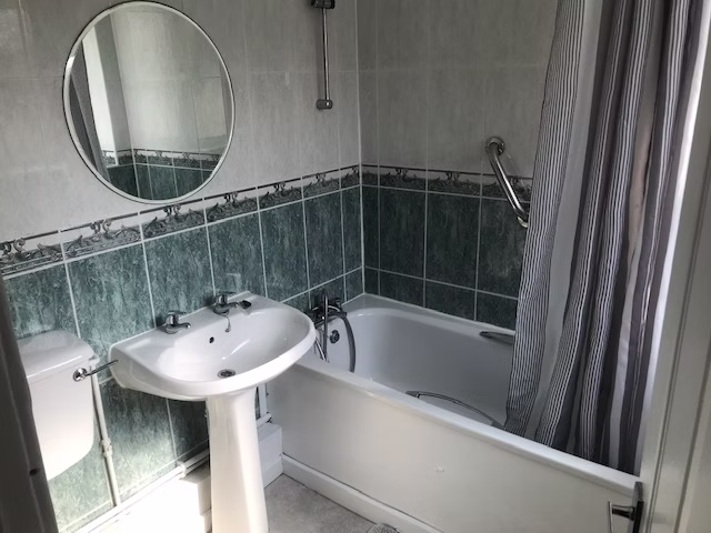 Bathroom with green tiled walls, white sink, toilet and bathtub with shower curtain